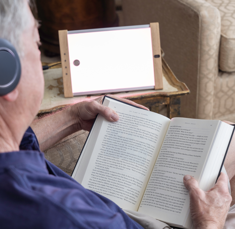 Man sitting in a chair reading in front of a light device. Photo: OptoCeutics