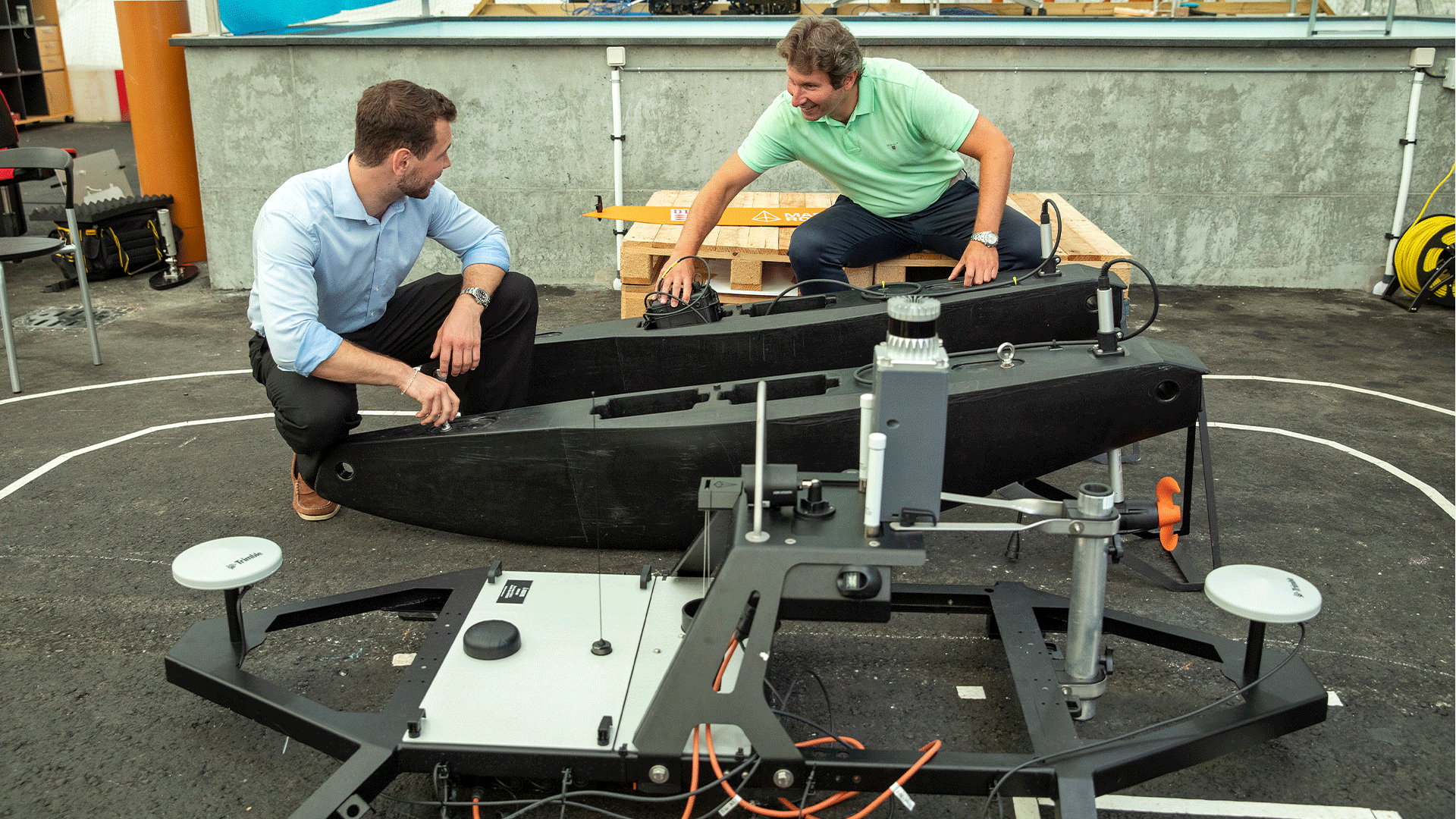 Two men crouched down while inspecting an autonomous marine vehicle.
