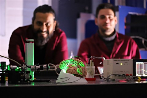 In-lab demonstration of an optical fiber implant on a brain model with green lighting, Christos Markos and Marcello Meneghetti in the background